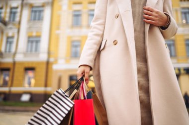 Alışveriş torbaları ellerde. Çok renkli çantaları ve alışverişleri olan genç bir kadının eli. Şehir caddesinde alışveriş torbaları tutan güzel bir kız. Tüketim, alışveriş, satış, yaşam tarzı konsepti. 