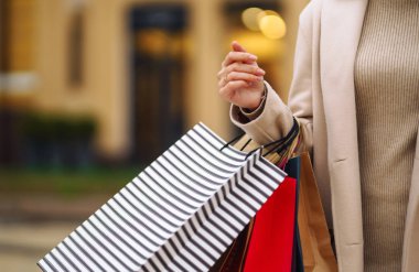 Telefonu ve kredi kartı olan güzel bir kadının elleri. Şehir caddesinde alışveriş torbaları tutan genç bir kadın. İnternetten alışveriş konsepti. Tüketim, satın alma, alışveriş, yaşam tarzı konsepti.