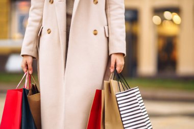Telefonu ve kredi kartı olan güzel bir kadının elleri. Şehir caddesinde alışveriş torbaları tutan genç bir kadın. İnternetten alışveriş konsepti. Tüketim, satın alma, alışveriş, yaşam tarzı konsepti.