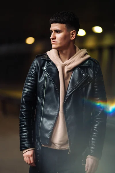 Portrait of a stylish man in the black jacket in tunnel. Young man  stands in a light tunnel and looks away. Fashion, lifestyle concept.