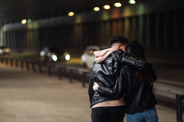 Back view of young couple  holding hand going through a dark tunnel. Stylish couple in love hug each other on the black background with lights. Together. Love, romantic, tenderness concept.