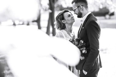 Gelin ve damadın güzel siyah beyaz fotoğrafı. Mutlu çift parkta gelinlik ve takım elbiseyle poz veriyor ve gülümsüyor. İnsanlar birbirlerinden hoşlanırlar. Birlikte. Düğün konsepti.