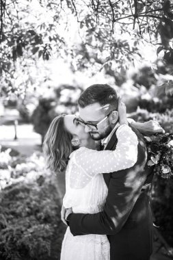 Gelin ve damadın güzel siyah beyaz fotoğrafı. Mutlu çift parkta gelinlik ve takım elbiseyle poz veriyor ve gülümsüyor. İnsanlar birbirlerinden hoşlanırlar. Birlikte. Düğün konsepti.