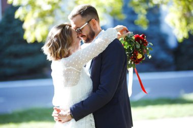 Genç çift parkta yürürken romantik anların tadını çıkarıyor. Gelin ve damat düğün günlerinde parkta poz verip öpüşüyorlar. Güzel beyaz elbiseli zarif gelin, takım elbiseli damat..