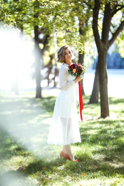 漂亮的新娘带着结婚花束在公园散步 穿着时髦的白色连衣裙的年轻新娘非常快乐 具有专业化妆和发型的优雅女人 婚礼日 — 图库照片