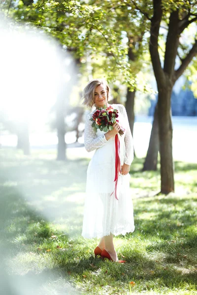 Beautiful bride with a wedding bouquet for a walk in the park. Young bride in the fashionable white dress is incredibly happy. Elegant woman with professional make up and hair style. Wedding day.