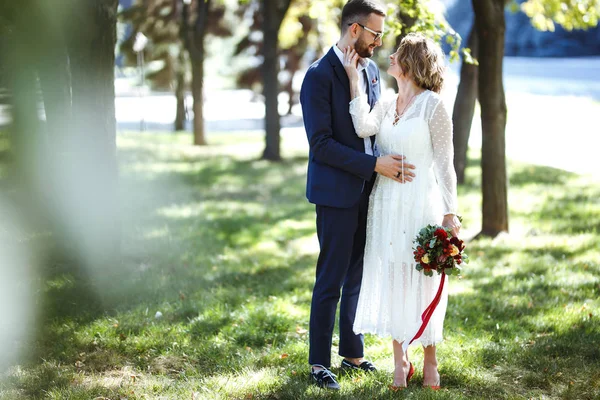 这对年轻夫妇在公园散步时享受着浪漫的时光 婚礼当天 时尚的新娘和新郎在公园里摆姿势接吻 漂亮的新娘穿着漂亮的白衣新郎穿着西服 — 图库照片
