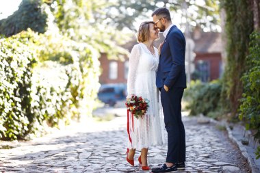 Genç çift yürürken romantik anların tadını çıkarıyor. Gelin ve damat düğün günlerinde parkta poz verip öpüşüyorlar. Güzel beyaz elbiseli zarif gelin, takım elbiseli damat. Birlikte.