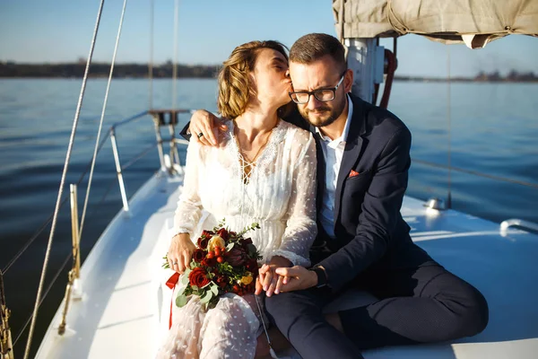 美丽的新婚夫妇在海上的婚宴上坐在游艇上 漂漂亮亮的新娘身穿白色婚纱 穿着时髦的新郎乘坐豪华游艇在海上航行 在一起 婚礼日 — 图库照片