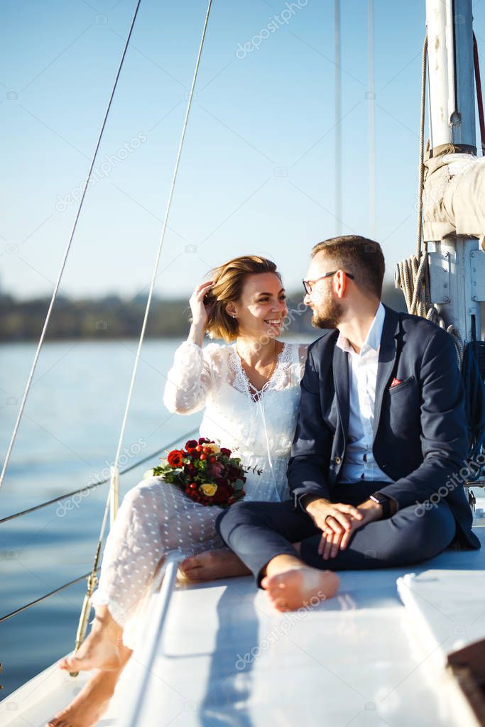 Beautiful wedding couple on yacht at wedding day outdoors in the sea. Beautiful elegant  bride in a white dress and stylish groom on the luxury yacht sailing down the sea. Together. Wedding day.