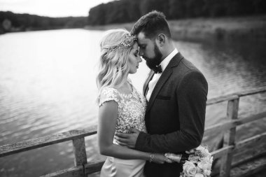 Siyah-beyaz, yeni evli çiftin düğün günü köprüde poz vermesini sağlıyor. Yakışıklı sakallı damat güzel gelini takdir eder ve öper. Birlikte. Gençlik, aşk, moda ve yaşam tarzı kavramı.