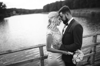 Siyah-beyaz, yeni evli çiftin düğün günü köprüde poz vermesini sağlıyor. Yakışıklı sakallı damat güzel gelini takdir eder ve öper. Birlikte. Gençlik, aşk, moda ve yaşam tarzı kavramı.