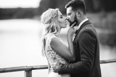 Siyah-beyaz, yeni evli çiftin düğün günü köprüde poz vermesini sağlıyor. Yakışıklı sakallı damat güzel gelini takdir eder ve öper. Birlikte. Gençlik, aşk, moda ve yaşam tarzı kavramı.