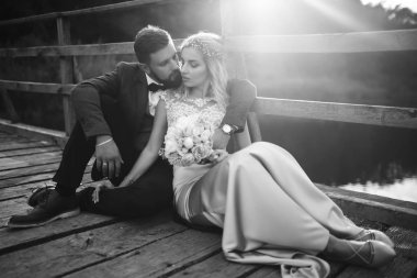 Siyah-beyaz, yeni evli çiftin düğün günü köprüde poz vermesini sağlıyor. Yakışıklı sakallı damat güzel gelini takdir eder ve öper. Birlikte. Gençlik, aşk, moda ve yaşam tarzı kavramı.