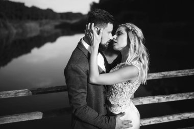 Siyah-beyaz, yeni evli çiftin düğün günü köprüde poz vermesini sağlıyor. Yakışıklı sakallı damat güzel gelini takdir eder ve öper. Birlikte. Gençlik, aşk, moda ve yaşam tarzı kavramı.