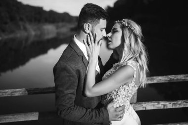 Siyah-beyaz, yeni evli çiftin düğün günü köprüde poz vermesini sağlıyor. Yakışıklı sakallı damat güzel gelini takdir eder ve öper. Birlikte. Gençlik, aşk, moda ve yaşam tarzı kavramı.