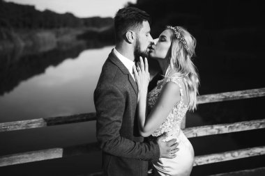 Siyah-beyaz, yeni evli çiftin düğün günü köprüde poz vermesini sağlıyor. Yakışıklı sakallı damat güzel gelini takdir eder ve öper. Birlikte. Gençlik, aşk, moda ve yaşam tarzı kavramı.
