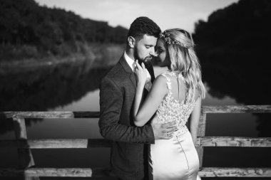 Siyah-beyaz, yeni evli çiftin düğün günü köprüde poz vermesini sağlıyor. Yakışıklı sakallı damat güzel gelini takdir eder ve öper. Birlikte. Gençlik, aşk, moda ve yaşam tarzı kavramı.
