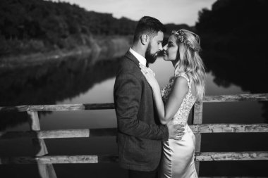 Siyah-beyaz, yeni evli çiftin düğün günü köprüde poz vermesini sağlıyor. Yakışıklı sakallı damat güzel gelini takdir eder ve öper. Birlikte. Gençlik, aşk, moda ve yaşam tarzı kavramı.
