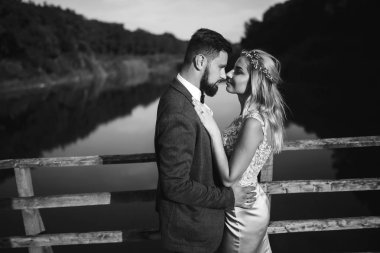 Siyah-beyaz, yeni evli çiftin düğün günü köprüde poz vermesini sağlıyor. Yakışıklı sakallı damat güzel gelini takdir eder ve öper. Birlikte. Gençlik, aşk, moda ve yaşam tarzı kavramı.