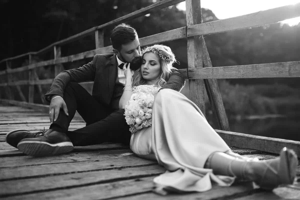 結婚式の日に橋の上にポーズをとっている黒と白の写真のスタイリッシュなカップル ハンサムなひげそりの新郎は賞賛し かなり花嫁のキス 一緒に若者 ファッション ライフスタイルの概念 — ストック写真