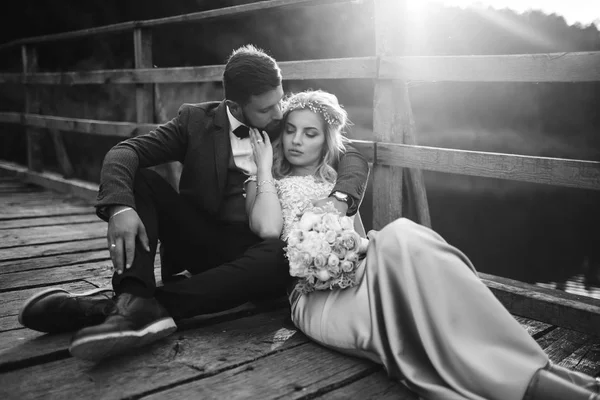 結婚式の日に橋の上にポーズをとっている黒と白の写真のスタイリッシュなカップル ハンサムなひげそりの新郎は賞賛し かなり花嫁のキス 一緒に若者 ファッション ライフスタイルの概念 — ストック写真