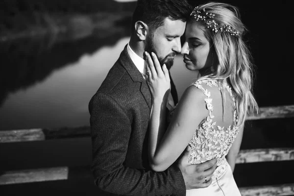 Siyah-beyaz, yeni evli çiftin düğün günü köprüde poz vermesini sağlıyor. Yakışıklı sakallı damat güzel gelini takdir eder ve öper. Birlikte. Gençlik, aşk, moda ve yaşam tarzı kavramı.