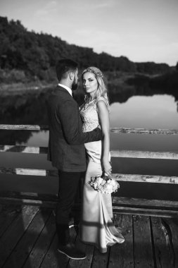 Siyah-beyaz, yeni evli çiftin düğün günü köprüde poz vermesini sağlıyor. Yakışıklı sakallı damat güzel gelini takdir eder ve öper. Birlikte. Gençlik, aşk, moda ve yaşam tarzı kavramı.