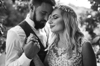 Gelin ve damadın şehvetli siyah beyaz foto 'su. Yeni evli çiftimiz düğün günlerinde parkta poz veriyormuş. Yakışıklı sakallı damat güzel gelini takdir eder ve öper. Birlikte.