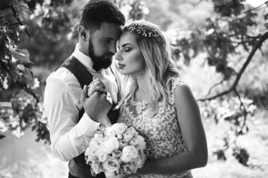 Gelin ve damadın şehvetli siyah beyaz foto 'su. Yeni evli çiftimiz düğün günlerinde parkta poz veriyormuş. Yakışıklı sakallı damat güzel gelini takdir eder ve öper. Birlikte.