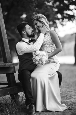 Gelin ve damadın şehvetli siyah beyaz foto 'su. Yeni evli çiftimiz düğün günlerinde parkta poz veriyormuş. Yakışıklı sakallı damat güzel gelini takdir eder ve öper. Birlikte.