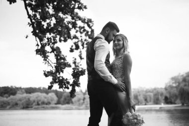 Gelin ve damadın şehvetli siyah beyaz foto 'su. Yeni evli çiftimiz düğün günlerinde parkta poz veriyormuş. Yakışıklı sakallı damat güzel gelini takdir eder ve öper. Birlikte.