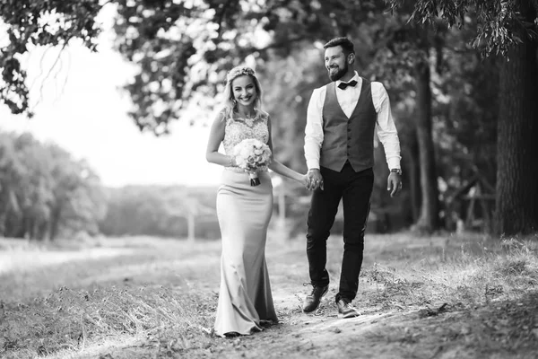 Sensual Black and white foto of bride and groom. Stylish couple of happy newlyweds posing in the park on their wedding day. Handsome bearded groom admires and kisses pretty bride. Together.