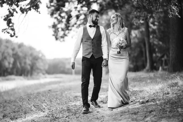 Sensual Black and white foto of bride and groom. Stylish couple of happy newlyweds posing in the park on their wedding day. Handsome bearded groom admires and kisses pretty bride. Together.