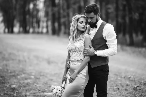 Sensual Black and white foto of bride and groom. Stylish couple of happy newlyweds posing in the park on their wedding day. Handsome bearded groom admires and kisses pretty bride. Together.