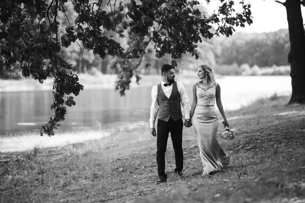 Sensual Black and white foto of bride and groom. Stylish couple of happy newlyweds posing in the park on their wedding day. Handsome bearded groom admires and kisses pretty bride. Together.