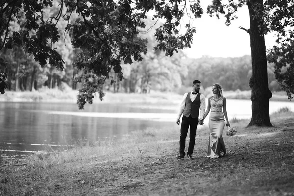 Sensual Black and white foto of bride and groom. Stylish couple of happy newlyweds posing in the park on their wedding day. Handsome bearded groom admires and kisses pretty bride. Together.