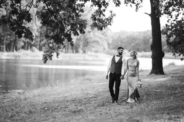 Sensual Black and white foto of bride and groom. Stylish couple of happy newlyweds posing in the park on their wedding day. Handsome bearded groom admires and kisses pretty bride. Together.