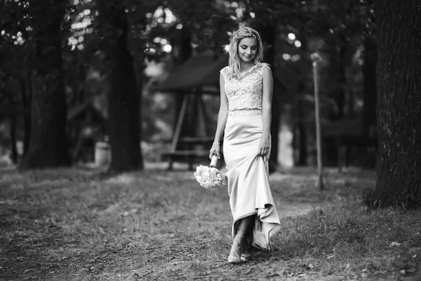 Black and white foto of beautiful bride with a wedding bouquet for a walk in the park. Happy newlywed woman stands among green bushes in the garden. Smiling bride. Wedding day. Fashion bride.