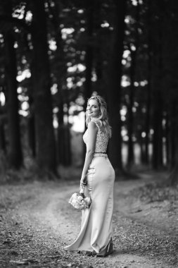 Parkta yürüyüş için bir buketi olan güzel gelinin siyah beyaz fotografı. Mutlu yeni evli kadın bahçedeki yeşil çalıların arasında duruyor. Gülümseyen gelin. Düğün günü. Moda Gelini.