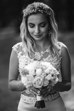 Siyah beyaz bir portre, zarif bir gelin ve bir düğün buketi. Güzel sarışın gelin bahçedeki yeşil çalıların arasında duruyor. Mutlu yeni evli kadın. Gülümseyen gelin. Düğün günü. Moda Gelini.