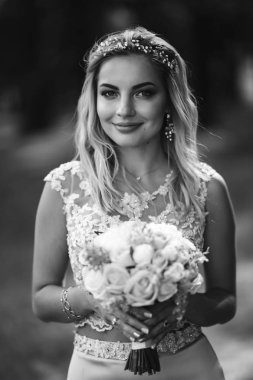 Siyah beyaz bir portre, zarif bir gelin ve bir düğün buketi. Güzel sarışın gelin bahçedeki yeşil çalıların arasında duruyor. Mutlu yeni evli kadın. Gülümseyen gelin. Düğün günü. Moda Gelini.