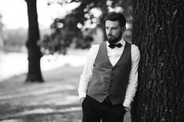 Siyah takım elbiseli, papyonlu, parkta poz veren yakışıklı bir adamın siyah beyaz portresi. Takım elbiseli lüks damat. İş adamı. Yeni evli mutlu bir damat. Düğün gününde zengin bir adam.. 