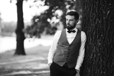 Siyah takım elbiseli, papyonlu, parkta poz veren yakışıklı bir adamın siyah beyaz portresi. Takım elbiseli lüks damat. İş adamı. Yeni evli mutlu bir damat. Düğün gününde zengin bir adam.. 