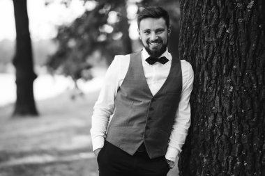 Siyah takım elbiseli, papyonlu, parkta poz veren yakışıklı bir adamın siyah beyaz portresi. Takım elbiseli lüks damat. İş adamı. Yeni evli mutlu bir damat. Düğün gününde zengin bir adam.. 