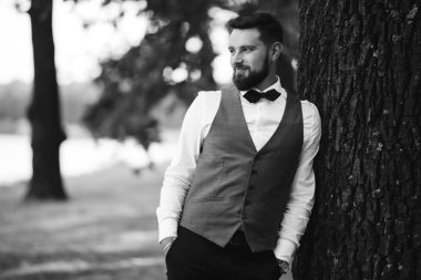 Siyah takım elbiseli, papyonlu, parkta poz veren yakışıklı bir adamın siyah beyaz portresi. Takım elbiseli lüks damat. İş adamı. Yeni evli mutlu bir damat. Düğün gününde zengin bir adam.. 