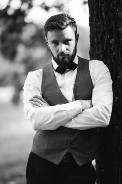 Siyah takım elbiseli, papyonlu, parkta poz veren yakışıklı bir adamın siyah beyaz portresi. Takım elbiseli lüks damat. İş adamı. Yeni evli mutlu bir damat. Düğün gününde zengin bir adam.. 