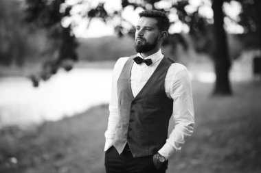 Siyah takım elbiseli, papyonlu, parkta poz veren yakışıklı bir adamın siyah beyaz portresi. Takım elbiseli lüks damat. İş adamı. Yeni evli mutlu bir damat. Düğün gününde zengin bir adam.. 