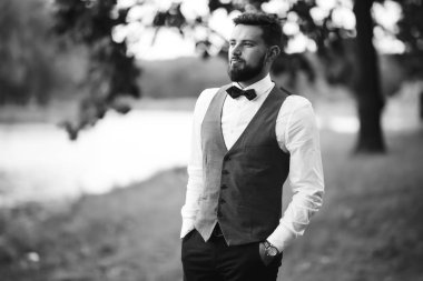 Siyah takım elbiseli, papyonlu, parkta poz veren yakışıklı bir adamın siyah beyaz portresi. Takım elbiseli lüks damat. İş adamı. Yeni evli mutlu bir damat. Düğün gününde zengin bir adam.. 