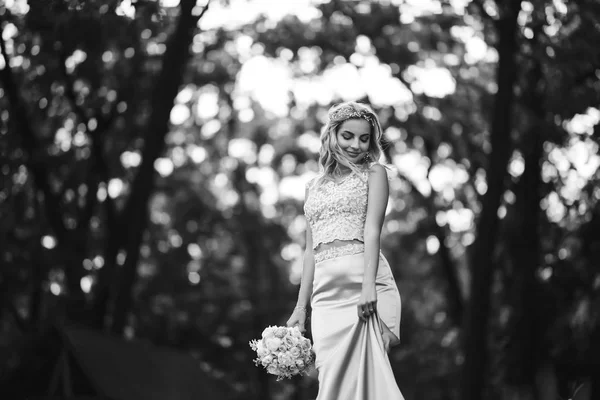 Black and white foto of beautiful bride with a wedding bouquet for a walk in the park. Happy newlywed woman stands among green bushes in the garden. Smiling bride. Wedding day. Fashion bride.